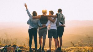 Cuatro personas abrazadas mirando el horizonte, disfrutando de un atardecer en la cima de una montaña. Representa la importancia del apoyo social en la construcción de la autoestima.