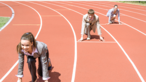 Personas en trajes de negocios en posición de salida en una pista de atletismo, simbolizando la competencia profesional y la determinación para alcanzar el éxito.